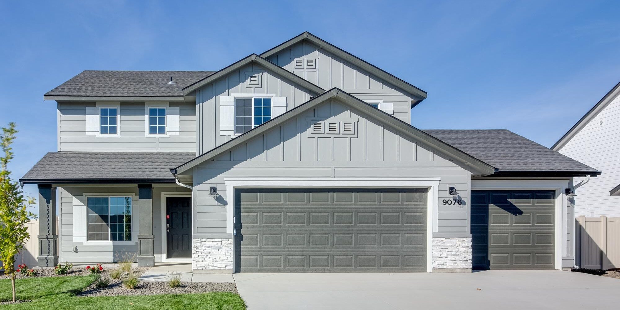 New two-story CBH Home with a three-car garage, modern gray siding, white trim, and a landscaped front yard in Idaho. This beautifully designed home features a covered front porch, black entry door, and large energy-efficient windows, offering curb appeal and contemporary living.